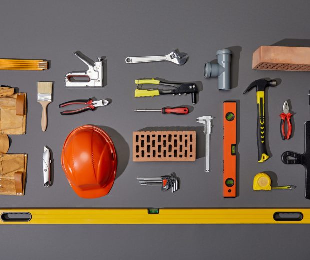 flat lay with bricks, orange helmet, tool belt and industrial tools on grey background