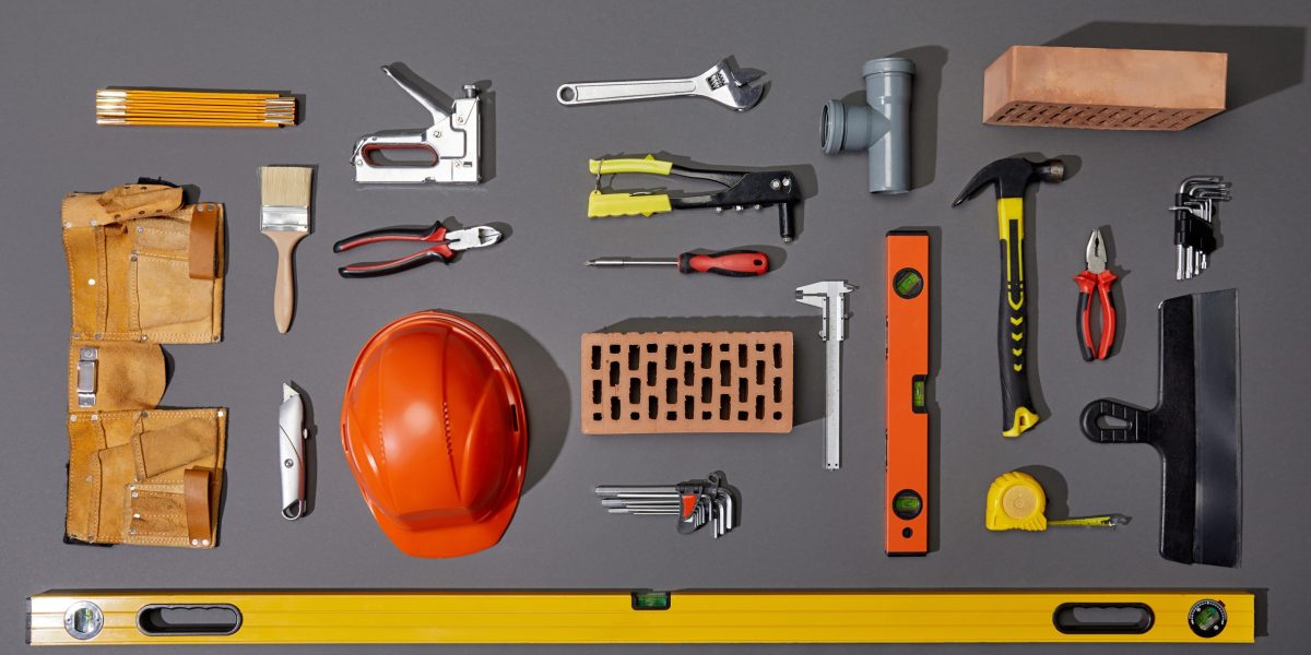 flat lay with bricks, orange helmet, tool belt and industrial tools on grey background